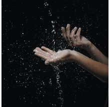 Nahaufnahme von Händen, die einen Wasserstrahl auffangen, mit zahlreichen Wassertropfen und Spritzern.