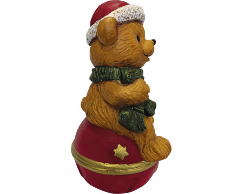 Weihnachtsfigur Teddybär mit Weihnachtsmütze und Schal sitzend auf einer roten Weihnachtskugel mit goldenem Stern.