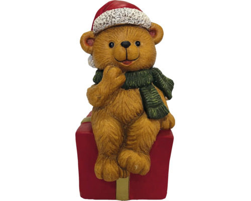 Weihnachts-Teddybär mit Nikolausmütze und Schal auf einem Geschenkpaket sitzend