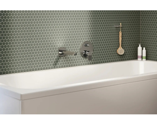 Modernes Badezimmer mit grünen Mosaikfliesen in Wabenoptik an der Wand hinter einer weißen Badewanne mit verchromten Armaturen.