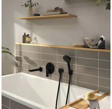 Moderne Badewanne mit mattschwarzen Unterputz-Armaturen, grauen Fliesen und Holzregalen mit Badaccessoires.