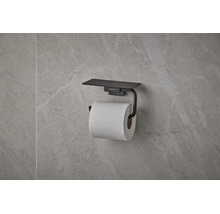 Mattschwarzer hansgrohe Toilettenpapierhalter mit Ablage, an einer Wand mit Natursteinoptik montiert.
