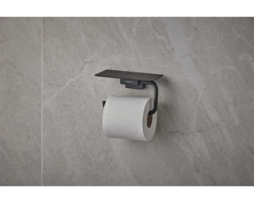 Mattschwarzer hansgrohe Toilettenpapierhalter mit Ablage, an einer Wand mit Natursteinoptik montiert.
