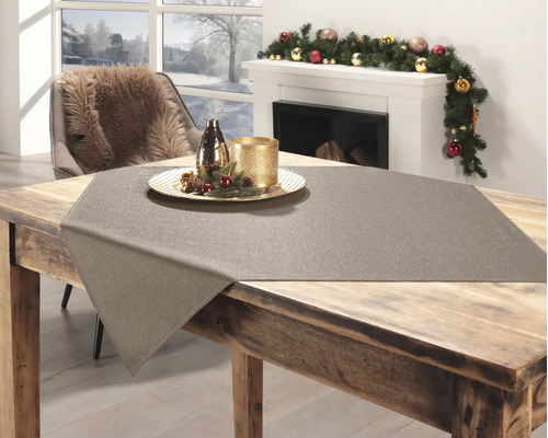 Glitzernde Mitteldecke auf einem Holztisch in einem hellen, winterlich dekorierten Raum mit Kamin und Weihnachtsguirlande.