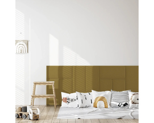 Gepolsterte Wandpaneele in Senfgelb als Kopfteil in einem hellen Kinderzimmer mit Deko-Kissen und Holzspielzeug auf hellem Holzboden.