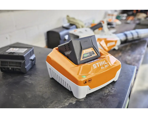 STIHL Schnellladegerät AL 301 mit eingesetztem Akku AK 30 auf einer Werkbank in einer Werkstatt.