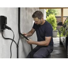 Ein Mann installiert einen schwarzen Wellschlauch als Kabelschutz für eine Wallbox Ladestation an einer Wand in einem Carport.