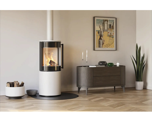 Moderner, weißer Kaminofen mit brennendem Holzfeuer in einem hellen Wohnzimmer mit Parkettboden, Sideboard und einer Zimmerpflanze.