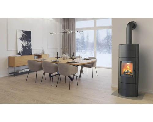 Moderner Wohn- und Essbereich mit einem brennenden schwarzen Kaminofen, einem großen Holztisch mit Polsterstühlen und hellem Ambiente.