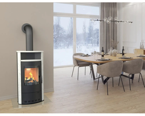 Moderner Kaminofen in Schwarz mit weißer Steinverkleidung in einem hellen Esszimmer mit Blick auf eine Schneelandschaft.