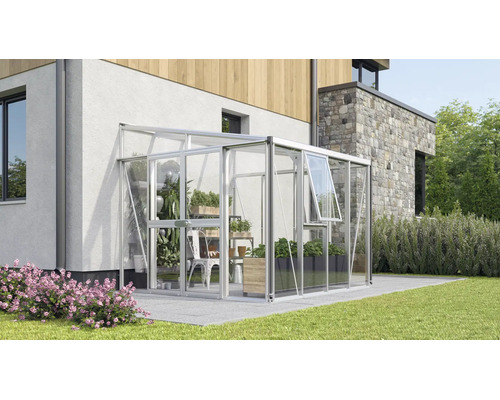 Modernes Anlehngewächshaus aus Aluminium und Glas, an einer Hauswand auf einer Terrasse mit Pflanzen im Inneren.