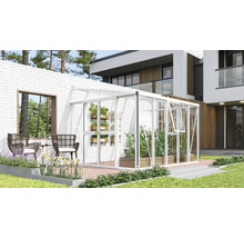 Weißes Anlehngewächshaus aus Aluminium und Glas an einer weißen Ziegelwand auf einer modernen Terrasse mit Pflanzen und Gartenmöbeln.
