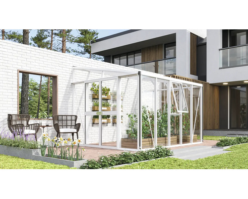 Weißes Anlehngewächshaus aus Aluminium und Glas an einer weißen Ziegelwand auf einer modernen Terrasse mit Pflanzen und Gartenmöbeln.