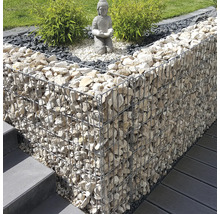 Moderne Gartengestaltung mit einer Gabionenmauer aus hellen Steinen, einer Buddha-Statue auf Kies und grünen Pflanzen neben Treppen und Terrasse.