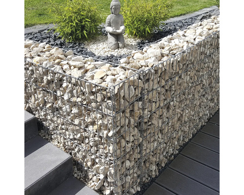 Moderne Gartengestaltung mit einer Gabionenmauer aus hellen Steinen, einer Buddha-Statue auf Kies und grünen Pflanzen neben Treppen und Terrasse.