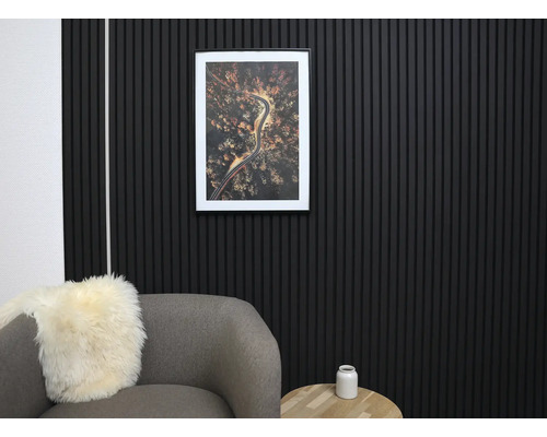 Moderne Wandgestaltung mit schwarzen Akustikpaneelen aus Holzlamellen in einem organisierten Wohnzimmer mit grauem Sessel und Holztisch.