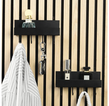 Zwei schwarze Metall-Wandregale mit Haken an einer hellen Holzlamellenwand, organisiert mit Parfüm, Schlüsseln und Kleidung in hellem Ambiente.