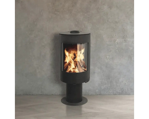 Moderner Kaminofen auf einem Standfuß mit brennendem Feuer hinter einer Glasscheibe vor einer Wand in Betonoptik.