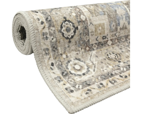Aufgerollter Kurzflorteppich mit orientalischem Vintage-Muster in Beige und Grau sowie einer gekettelten Kante.