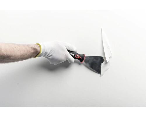 Hand mit Arbeitshandschuh nutzt einen Malerspachtel zum Entfernen von Tapete von einer Wand.