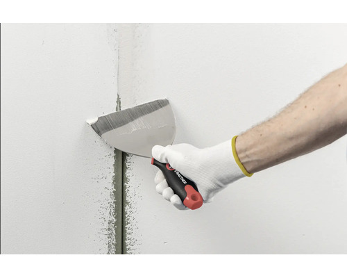 Hand mit Rautner Fassadenspachtel glättet Spachtelmasse über einer Fuge an einer Wand.