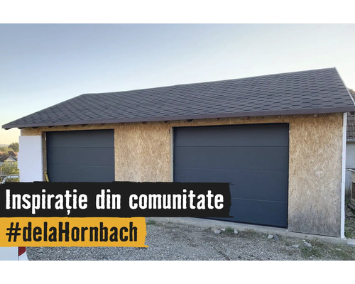 Doppelgarage im Bau mit OSB-Plattenwänden, zwei anthrazitfarbenen Sektionaltoren und einem dunklen Schindeldach.