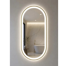 Ovaler Badspiegel mit Goldrahmen und LED-Beleuchtung. Im Spiegel spiegelt sich ein helles Badezimmer mit freistehender Wanne und Marmorwand.