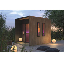 Moderne Garten-Sauna mit vertikaler Holzlamellen-Fassade und zwei schmalen Fenstern auf einer Holzterrasse im Außenbereich.