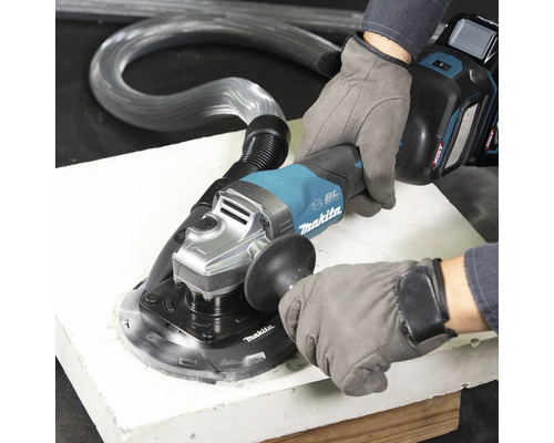 Eine Person in Arbeitshandschuhen bedient einen Akku-Winkelschleifer mit Absaughaube und Saugschlauch auf einer Platte. Makita Logo.