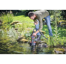 Ein Mann setzt eine Schmutzwassertauchpumpe in einen Gartenteich ein, um das Wasser abzupumpen.