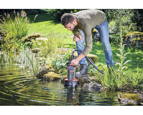 Ein Mann setzt eine Schmutzwassertauchpumpe in einen Gartenteich ein, um das Wasser abzupumpen.
