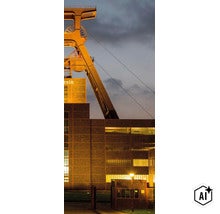Industriegebäude mit historischem Förderturm bei Dämmerung und Beleuchtung der Ziegelsteinfassade. (Image AI modified or generated)