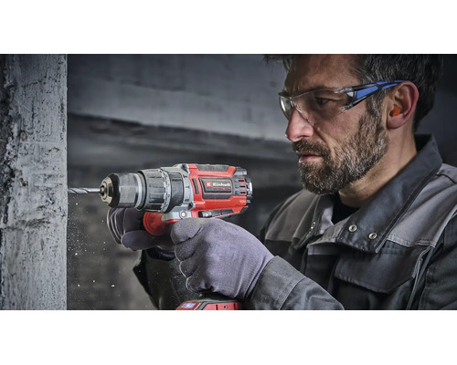 Handwerker mit Einhell Akku Schlagbohrschrauber beim Bohren in eine Betonwand mit Schutzbrille und Gehörschutz.