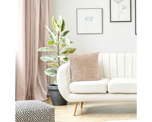 Wohnzimmer mit modernem Sofa, beigem Kissen, Zimmerpflanze und geometrischem Hocker in einer hellen und wohnlichen Einrichtung.