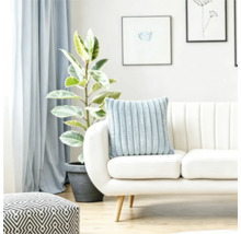 Ein weiches geripptes Kissen auf einem hellen Sofa in einem hellen Wohnzimmer mit einer Pflanze und geometrischem Hocker.