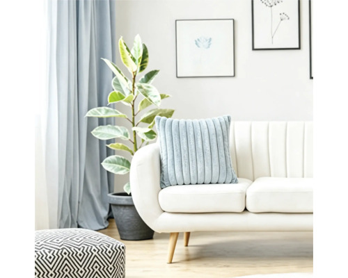 Ein weiches geripptes Kissen auf einem hellen Sofa in einem hellen Wohnzimmer mit einer Pflanze und geometrischem Hocker.