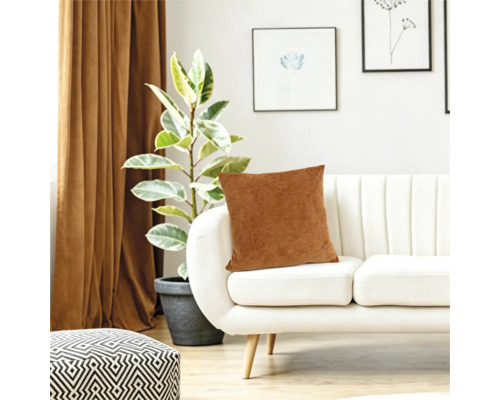 Ein Dekokissen auf einem modernen weißen Sofa im Wohnzimmer mit einer Topfpflanze und Vorhängen im Hintergrund.