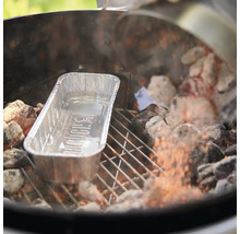 Eine Weber Grillschale aus Aluminium auf einem Holzkohlegrill zwischen glühenden Kohlen.