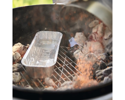 Eine Weber Grillschale aus Aluminium auf einem Holzkohlegrill zwischen glühenden Kohlen.