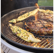 Ein Kugelgrill mit brennender Holzkohle, auf dem ein Rindersteak und gefüllte Maiskolben direkt über dem Feuer gegrillt werden.