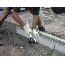 Ein Arbeiter verwendet einen Gummihammer, um eine Betonkante zu setzen.