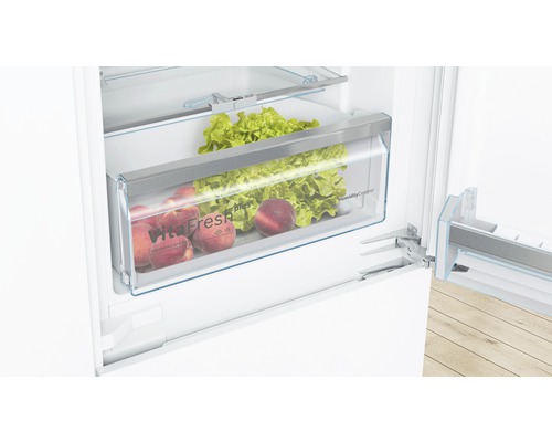 Geöffneter Kühlschrank mit Gemüsefach gefüllt mit Salat und Pfirsichen.
