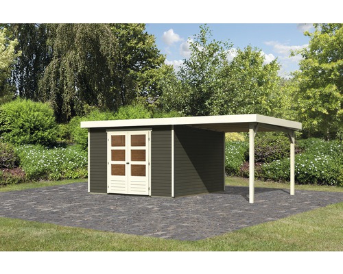 Gartenhaus Karibu Kodiak 6 inkl. Dachanbau 558 x 331 cm terragrau Gartenhaus mit Anbau auf gepflasterter Fläche in einem Garten.