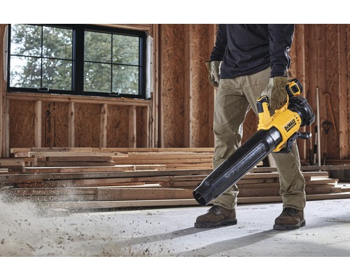 Ein Mann verwendet einen gelben und schwarzen Akku-Laubbläser von DeWalt auf einer Baustelle.