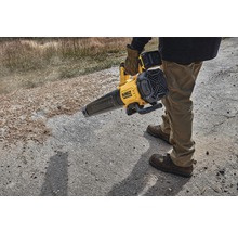 Eine Person bedient einen gelben Akku-Laubbläser von DeWalt auf einer unbefestigten Oberfläche.