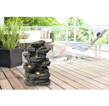 Dekorative Steinbrunnen-Szene auf einer Terrasse mit Gartenmöbeln und Pflanzen