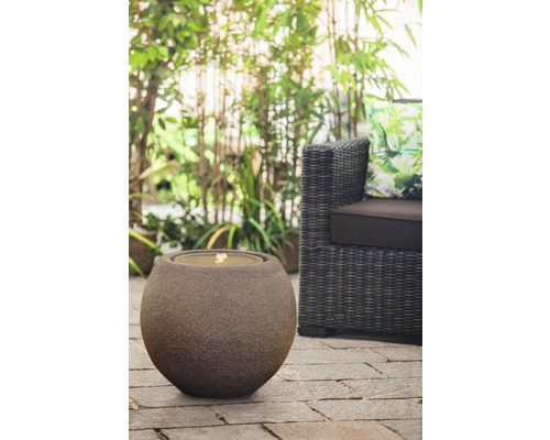 Dekorativer Kugelbrunnen aus Stein neben Korbsessel im Garten