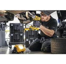 Mechaniker arbeitet mit einem Akku-Drehschlagschrauber an einem Auto, im Hintergrund Werkzeugkoffer und eine Arbeitsleuchte.