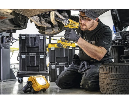 Mechaniker arbeitet mit einem Akku-Drehschlagschrauber an einem Auto, im Hintergrund Werkzeugkoffer und eine Arbeitsleuchte.