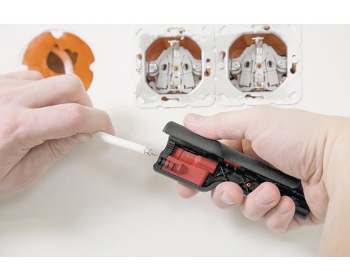 Ein Elektriker verwendet ein Abisolierwerkzeug, um ein Kabel für die Steckdose vorzubereiten.